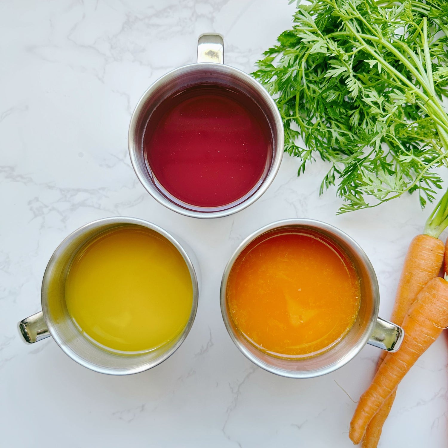 Top view of three 250ml stainless steel mugs filled with juice, with fresh carrots placed beside them on a table, showcasing eco-friendly drinkware for healthy meals.