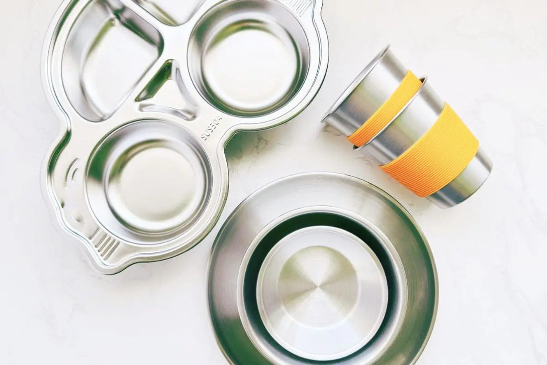 Top view of kids stainless steel divided plates, plates, bowls and cups with silicone sleeve, showcasing non-toxic eco-friendly dining essentials.