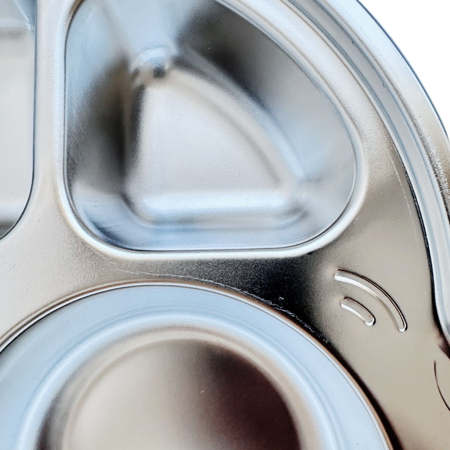 Close-up view of imperfections on a kid's stainless steel seconds car-shaped plate with suction.