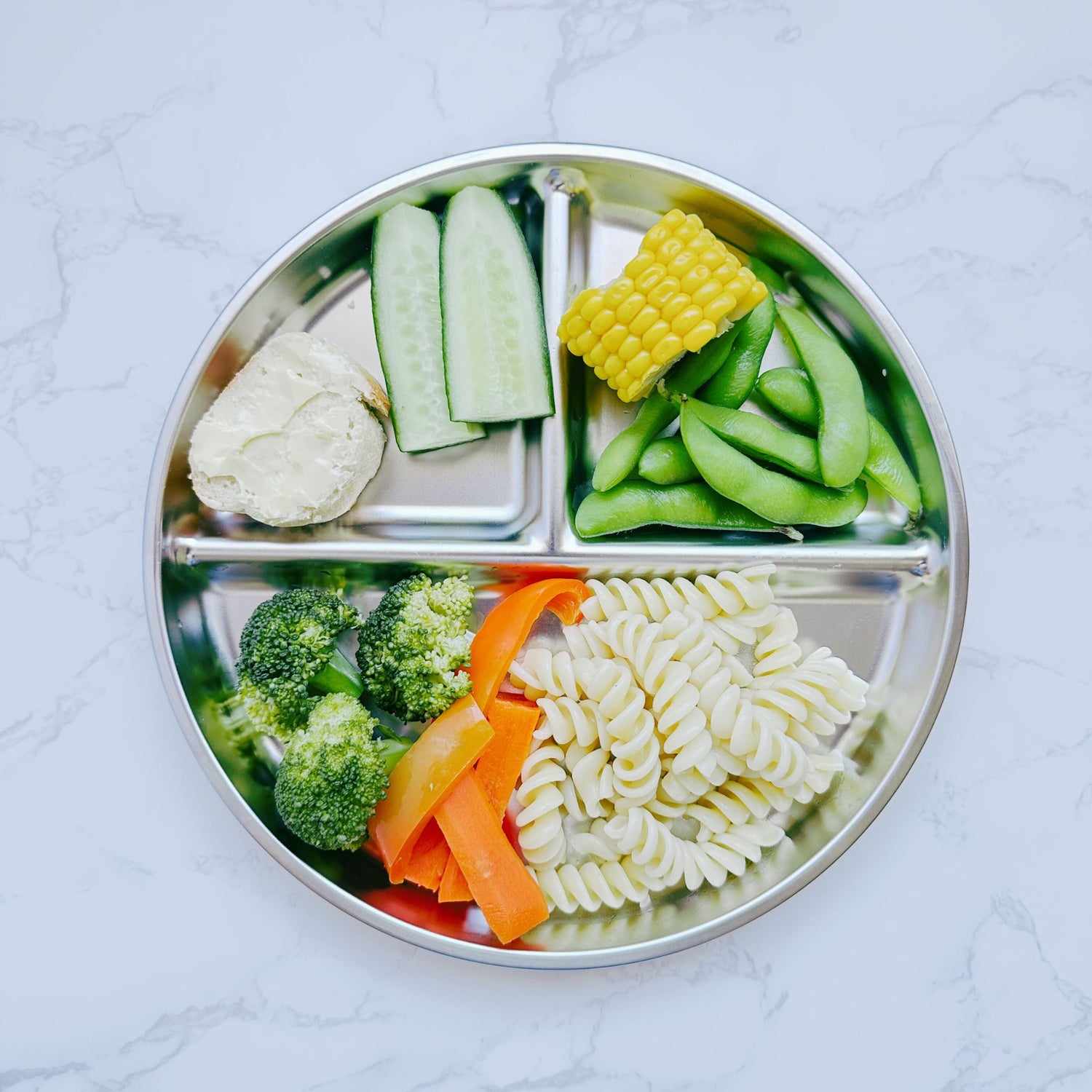 Top view of a kids' round stainless steel divided plate filled with food on a table, highlighting an eco-friendly and non-toxic mealtime solution.