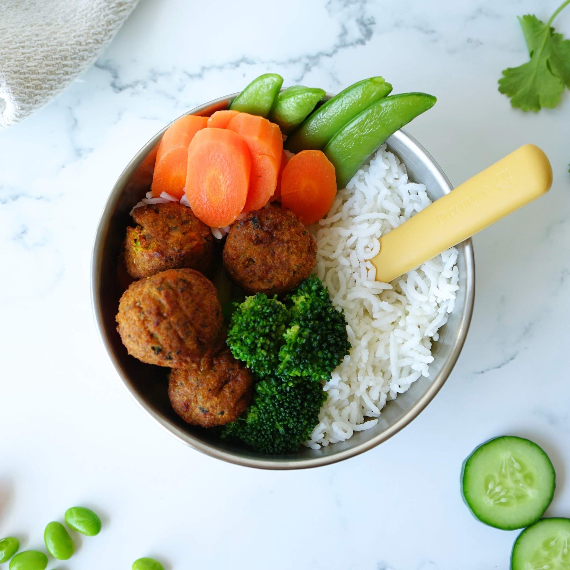 Greenvyne toddler and kids' spoon stainless steel with yellow silicone handle on a bowl with food.